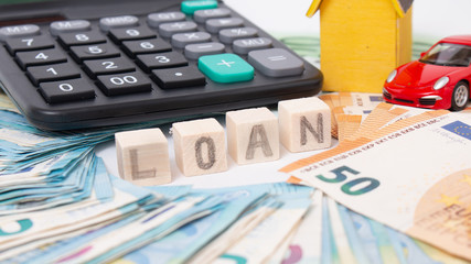 Finance and car loan, saving money for a car. Red car and euro banknotes. Calculator, euro money and House. Wooden cubes with word loan. Copy space for text. Loan payment car and house.