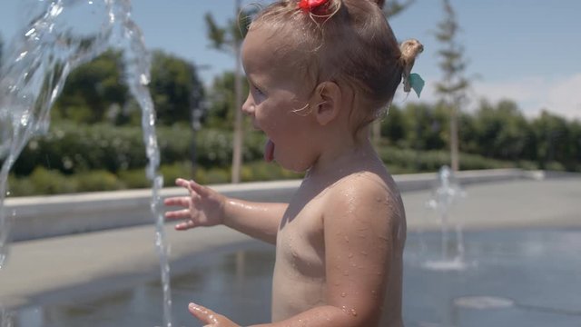 Funny two year old girl having water fun outdoors. Baby playing and refreshing with fountain jet