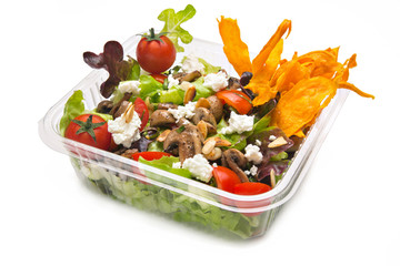 Healthy salad in plastic takeaway container. Goat cheese, tomato, mushrooms, assorted lettuce and sweet potato chips.