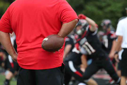 A High School Football Coach Warms Up Team Members Prior To A Game.