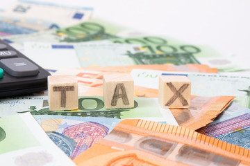 Taxes and spending concept. Tax word writen on wooden cubes. Euro banknotes Laid out in a semicicircle and calculator.Copy space for text. Euro money and calculator on white background.