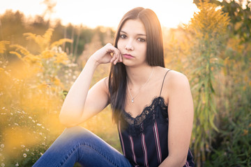 One young pretty woman sitting in a field in summertime at sunset. This field is filled with ragweed responsible for seasonal allergy.