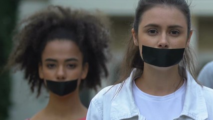 Female activists demonstrating with taped mouth, march against domestic violence