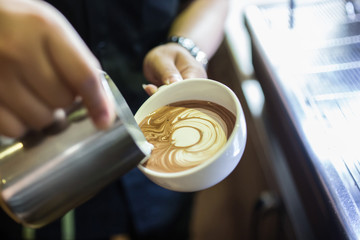 Barista at cafe making latte art with milk and coffee. Close up hand of barista pouring milk making latte art