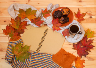 Naklejka na ściany i meble Empty notebook, mug of hot coffee, autumn maple leaves, muffins and warm homemade sweater on wooden surface.