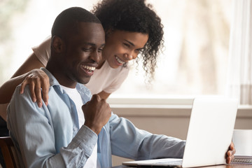 Excited biracial couple triumph win lottery on laptop online