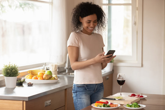 Smiling biracial woman texting on cell preparing food