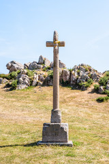 Eroded granite calvary of the chapel of Saint-Nicolas in Bugueles, Brittany, France, in front of a granite outcrop under a bright sunshine.