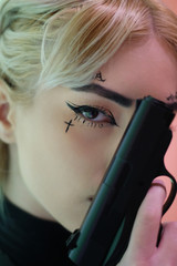 Fototapeta premium Portrait of a young blonde hair model holding a gun in studio, beautiful lights, makeup and eyes
