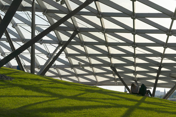 Fototapeta premium Modern ceiling with glass elements, metal mesh with green grass. Blue sky and green landscape. Zaryadye modern park in Moscow. Futuristic metal and glass.