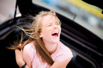 Fototapeta na wymiar the girl sits in the car on a summer day and laughs out loud, squinting her eyes. Warm positive weekend