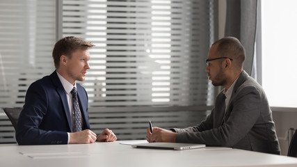 Two multiracial focused male partners discussing company development strategy.