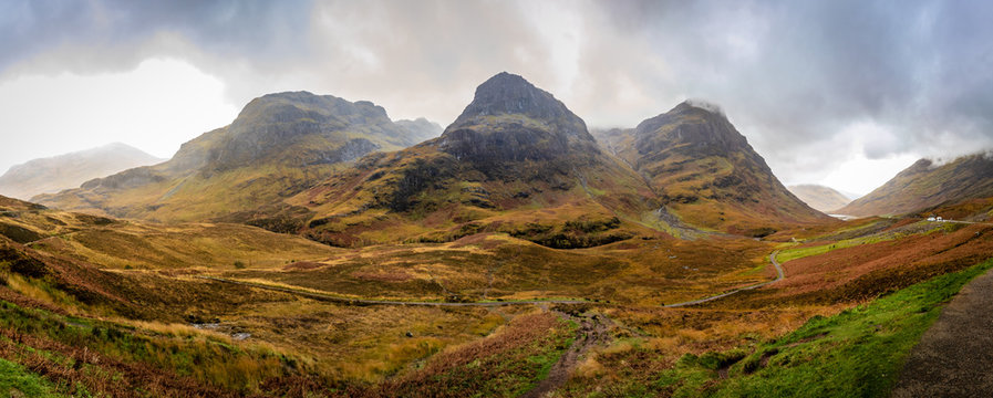 Panoramic view of steep mountains in the center and valleys on both sides with bright green and orange on an overcast afternoon in Glencoe, Highland, Scotland, United Kingdom