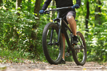 Fototapeta na wymiar Sporty body of young cyclist riding bike down the woods