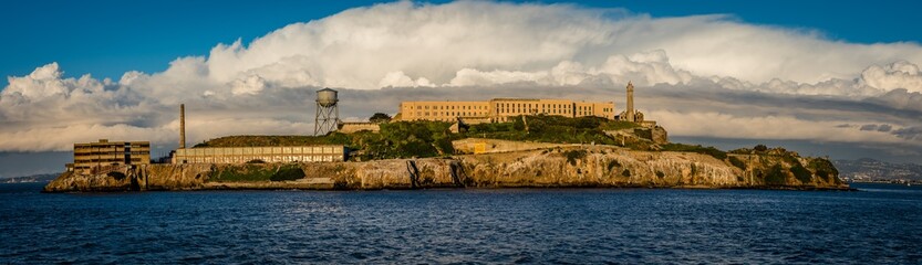 Panorama of Alcatraz Island with grand white clouds behind the old buildings on the hard rock