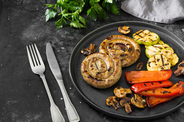 Grilled sausages on a black plate on a dark background