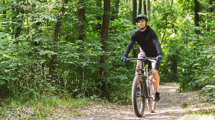 Fototapeta na wymiar Relaxed sportsman enjoying cycling down forest trail