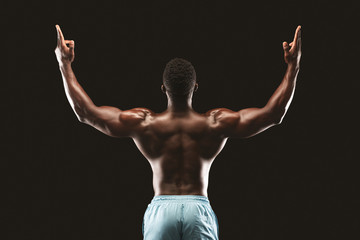 Back view of african bodybuilder raising his hands up - obrazy, fototapety, plakaty