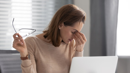 Exhausted female employee took off glasses, feeling pain in eyes.