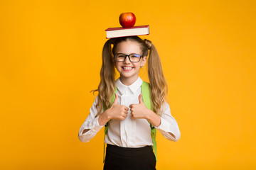 Schoolgirl Gesturing Thumbs-Up Holding Book And Apple On Head
