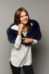 Beautiful and sexy young model woman, fashionable and happy beauty with bright makeup and shiny smile, in a fur scarf and a white blouse, smiling and posing at the grey background, isolated