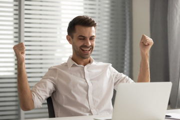 Young happy male employee celebrating job promotion at office.