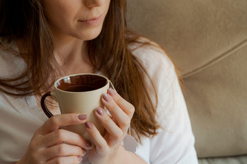 Detail of woman holding cup with tea. Beautiful woman sitting on the couch.
