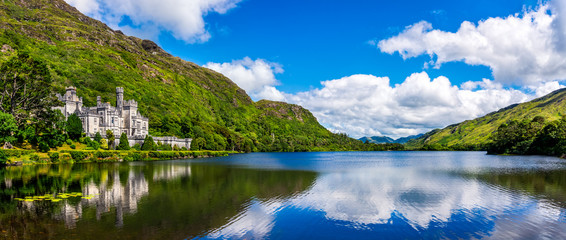 Panorama of Kylemore Abbey, beautiful castle like abbey reflected in lake at the foot of a mountain. Benedictine monastery, in Connemara, Ireland - obrazy, fototapety, plakaty