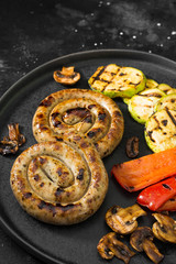 Grilled sausages on a black plate on a dark background