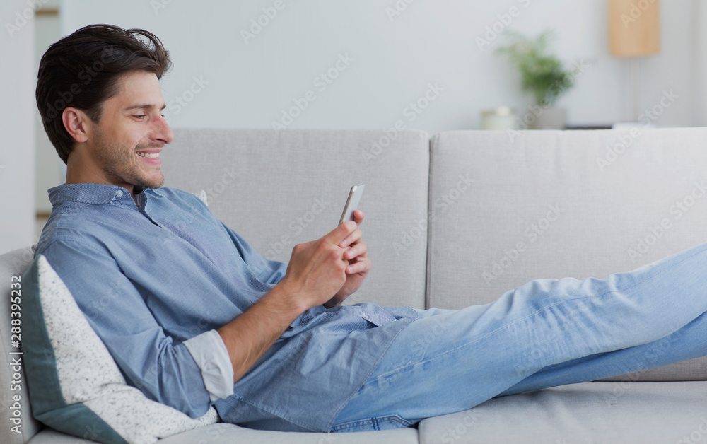Poster happy man using smartphone browsing internet lying on couch