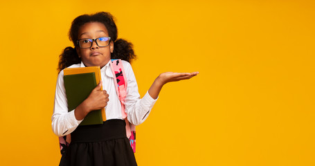 Puzzled School Girl Shrugging Shoulders Holding Books On Yellow Background