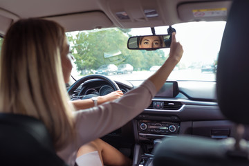 woman driving car, in summer city, rear-view mirror, parking car, reversing, looks back row seats, checks children on back sofa, controls back row of seats with passengers.
