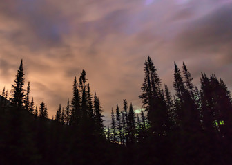 Aurora (Northern Lights) and stars over a calm forested mountain scene with orange, purple and green clouds.