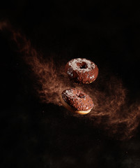 Chocolate doughnut with cocoa powder explosion in motion on a black background