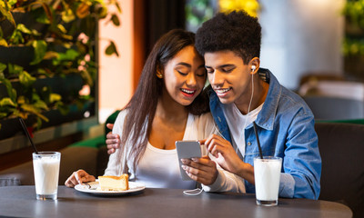 Couple of teenagers watching videos on phone in cafe
