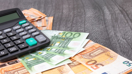 Calculator and euro money on grey wooden desk. Euro banknotes with black calculator on wooden background. Copy space for text. Finances and budget concept.