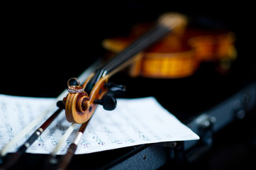 Naklejka premium wedding rings lie on the head of the neck of the violin against the background of musical notes. close-up