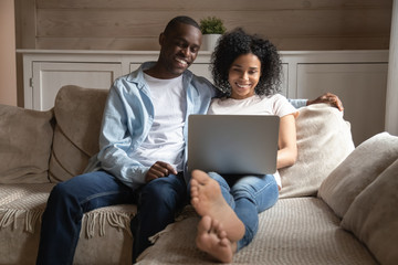 Happy biracial couple relax on couch using laptop
