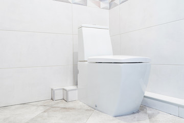 Naklejka na ściany i meble New modern ceramic toilet bowl near grey tiled wall in restroom.