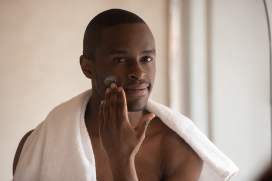 Young biracial man apply face cream after shower
