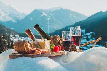 Traditional Italian food and drink outdoor in sunny winter day. Romantic alpine picnic in Madonna Di Campiglio with mountains background, Lambrusco cheese baguette tomatoes on the snow.