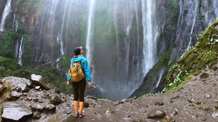 Woman walks through the waterfall, enjoying view on the waterfall Tumpak Sewu in Java island, Indonesia