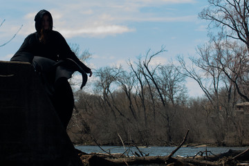 Hooded Woman in black robes in front of the Lake. Witches. Halloween and Gothic. Witchcraft and magic. Back to Nature concept.