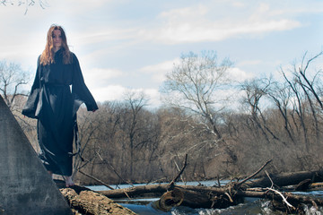 Woman with dark long hair in black robes in front of the Lake. Witches. Halloween and Gothic. Witchcraft and magic. Back to Nature concept.