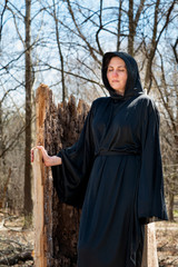 Hooded Woman in black robes deep in the Forest. Witches. Halloween and Gothic concept. Witchcraft and magic. Scary. 