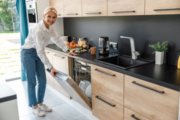 Happy woman opening door of the dishwasher