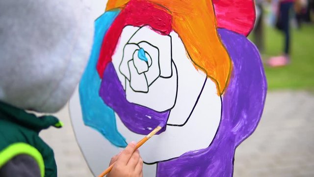 The boy paints a rose with a brush on holiday