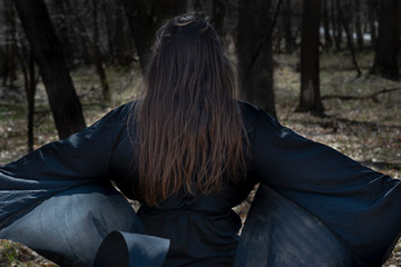 Young Woman with dark long hair in black robes deep in the Forest. Witches. Halloween and Gothic concept. Witchcraft and magic. 