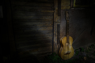 An wooden acoustic guitar is against a grunge textured wall. The room is dark with a spotlight for your copyspace.