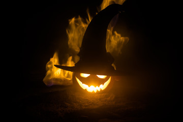 Fototapeta premium Halloween concept. Jack-o-lantern smile and scary eyes for party night. Close up view of scary pumpkin with witch hat on at dark foggy background. Selective focus.